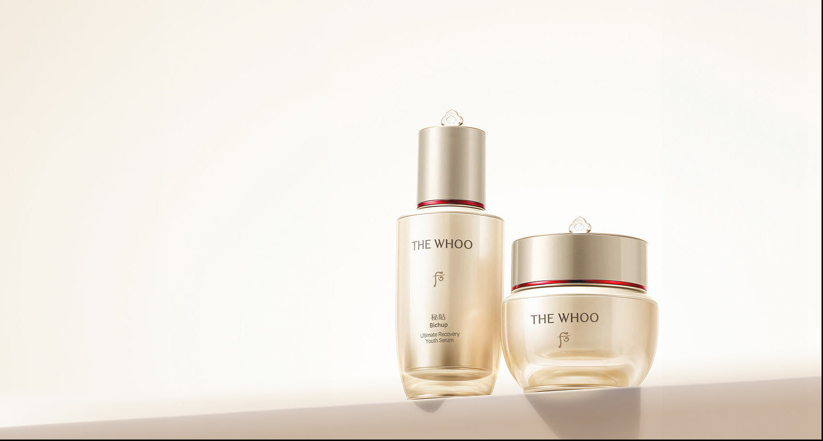 Two skincare products from The Whoo, including a glass bottle with a gold cap and a matching jar with a gold lid, set against a clean, warm off-white background.